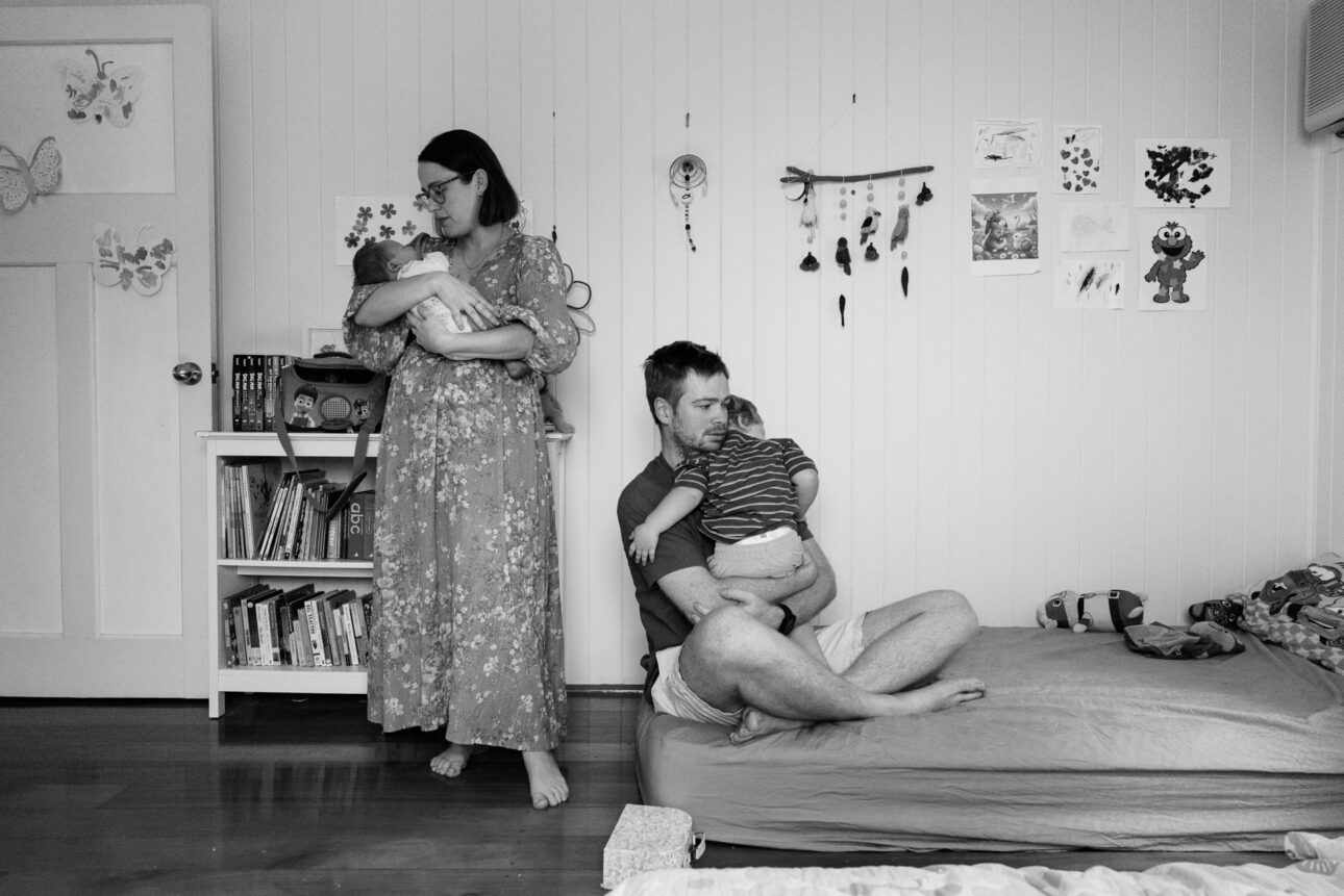 A mother is holding her newborn while the father is holding the toddler